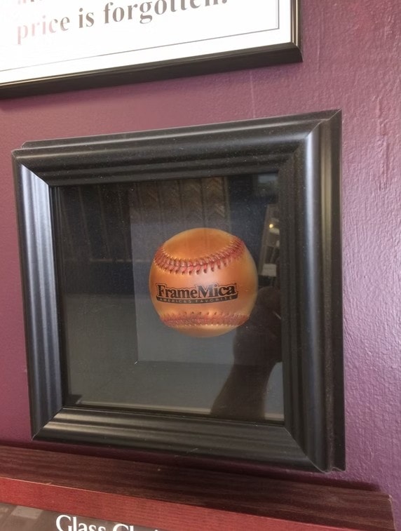 Framed FrameMica baseball displayed in a black shadow box on the shop wall